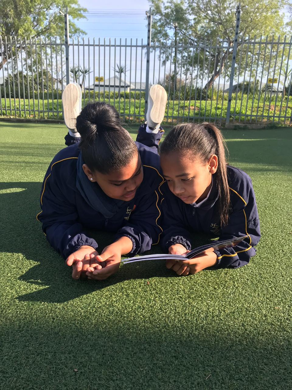 2 Mädchen in Schuluniform auf einer Wiese am Buch lesen.